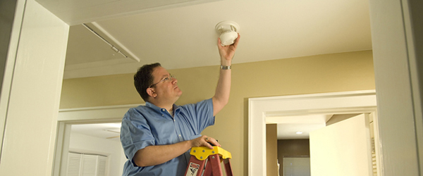 A handyman installs a smoke alarm for an elderly resident.