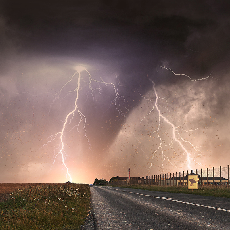 Un tornado y rayos se ven en la distancia de una carretera larga.  