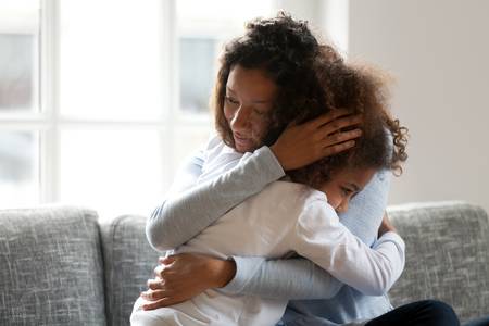 A mother is comforting her young daughter by giving her a hug