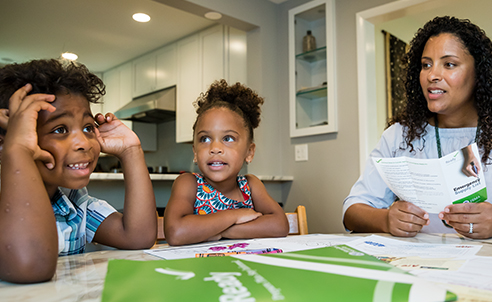 A woman is speaking with her two children at a table where Ready materials are spread out and being reviewed