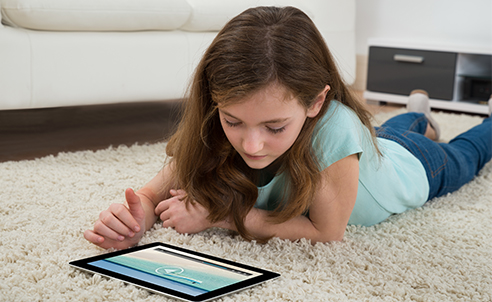 A girl laying on the floor looking at her tablet. 