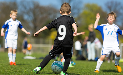 Three children playing soccer - one in a black jersey and is about to kick the ball from the two on the opposing team