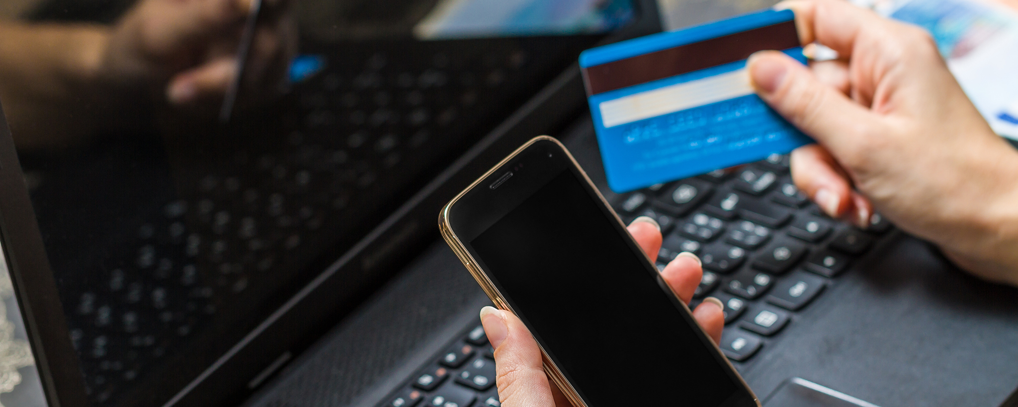 a man's hands holding a credit card and a mobile phone with a laptop