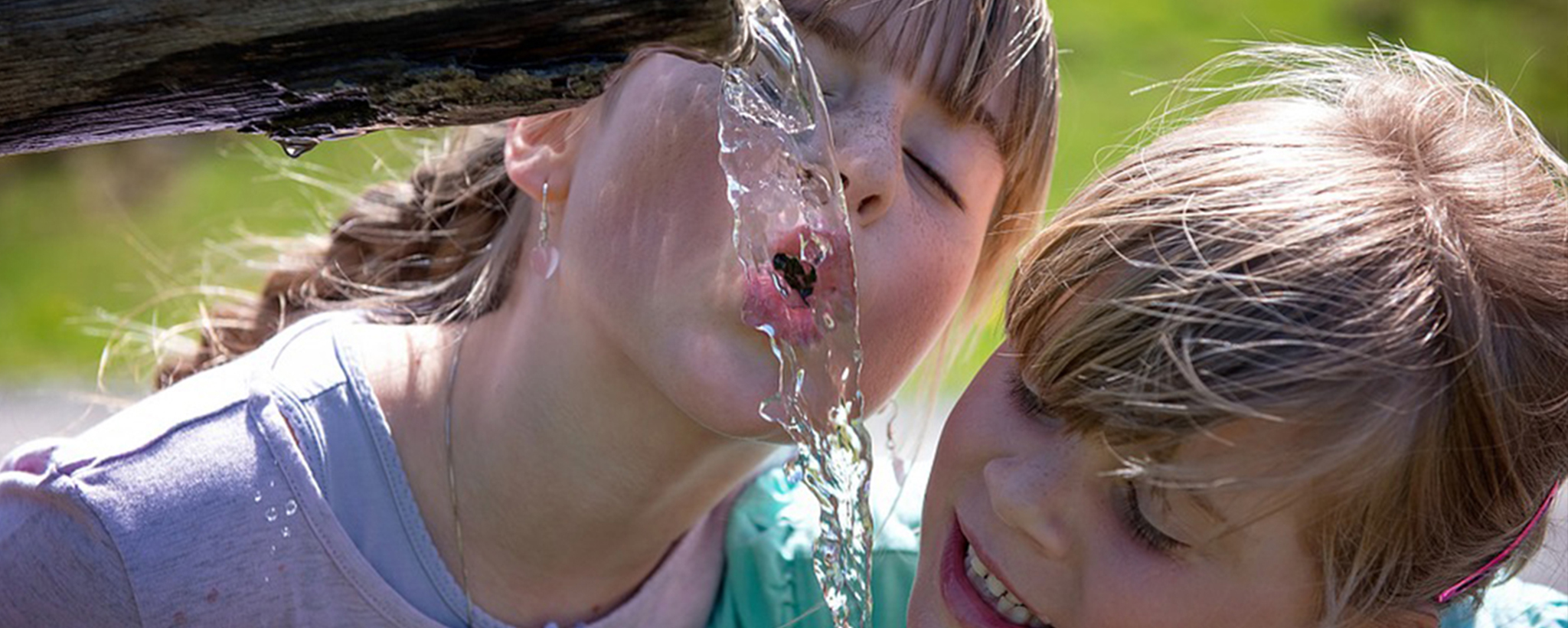 Two girls drink from a fountain on a hot day