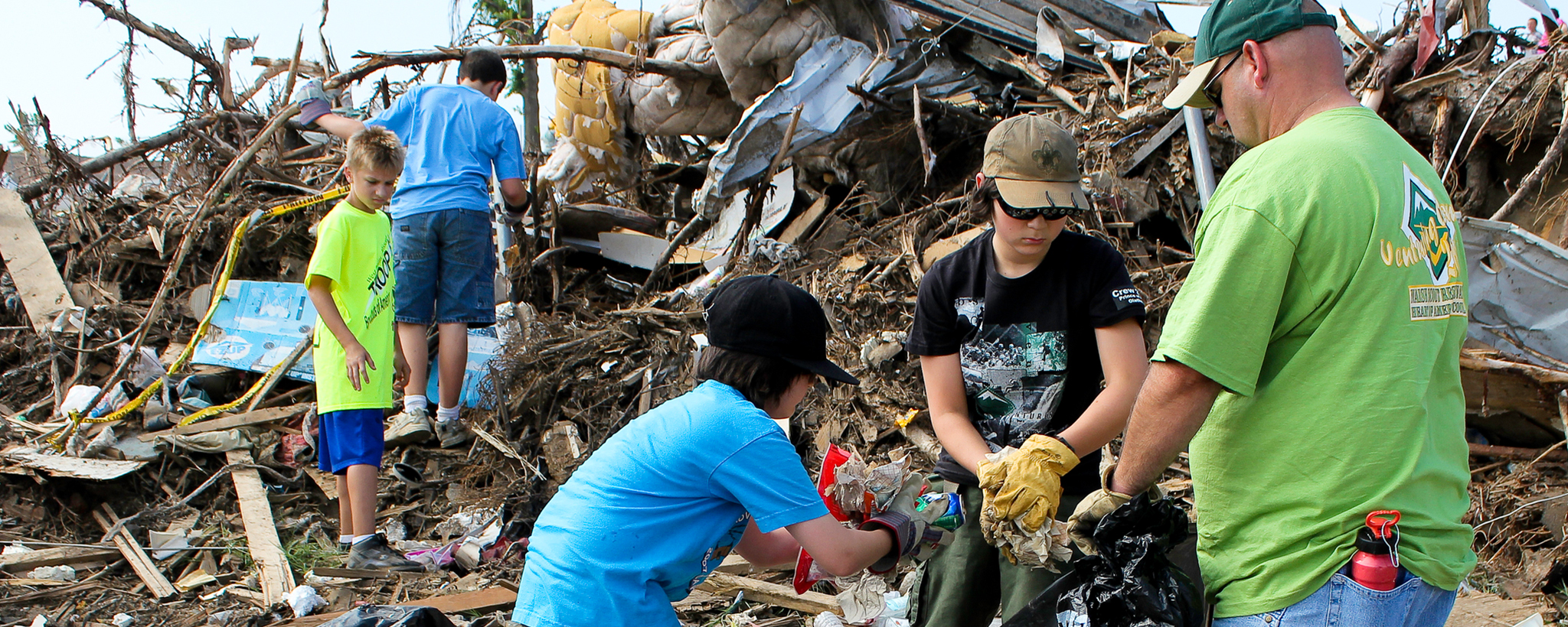 Four boy scouts with their leader engaging in a debris clean up while wearing gloves and other protective gear