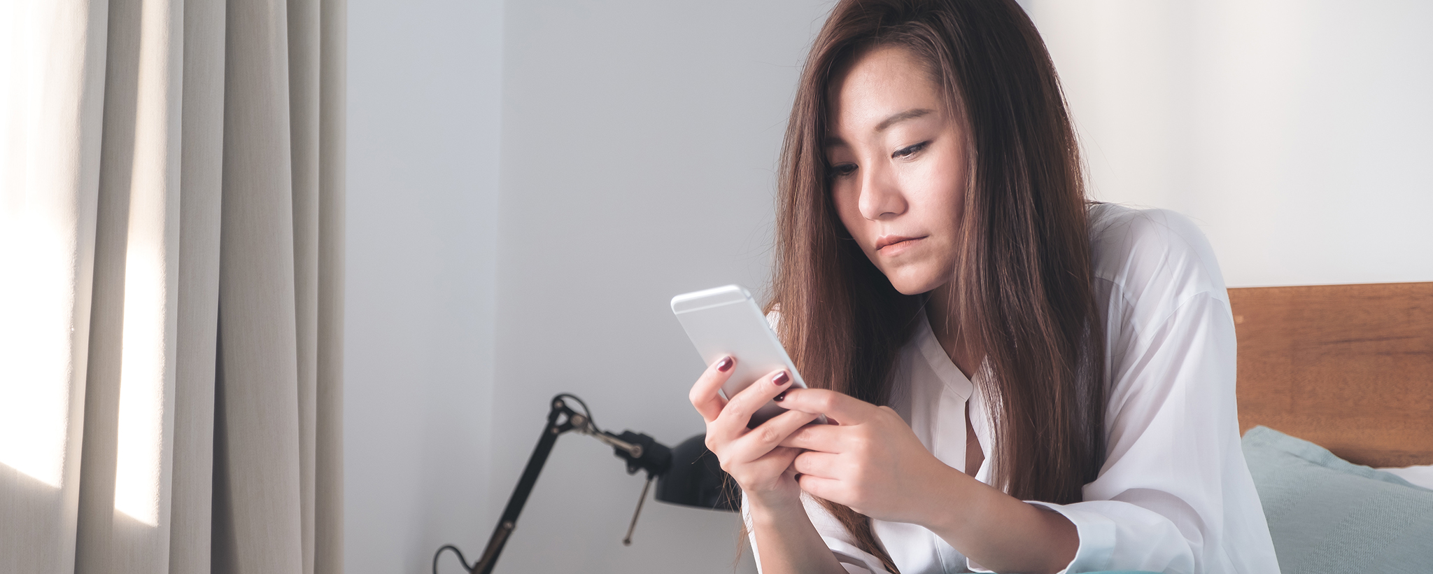 a woman sits on her bed looking at her smart phone