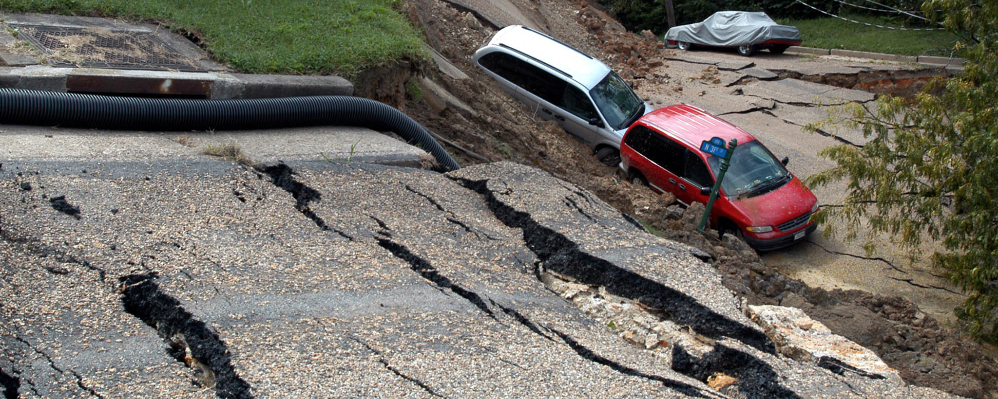 Two mini vans - one red and one white - are caught in a landslide and have fallen off the road