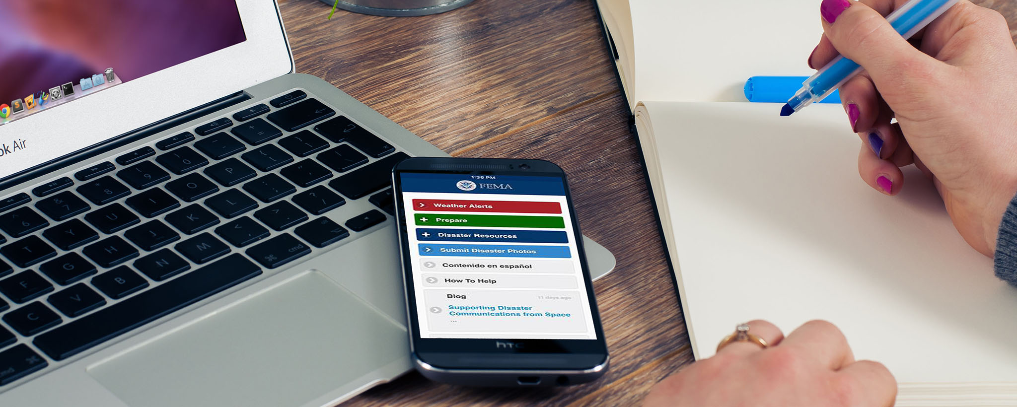 a smart phone with the fema app lays on the table. a person holds a pen and paper
