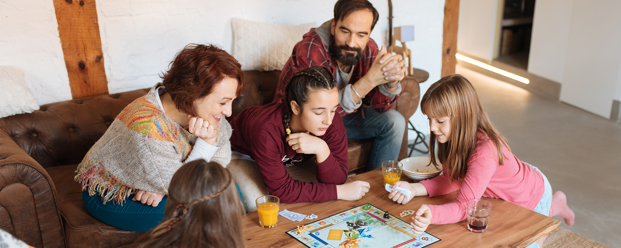 A family of five surrounding a coffee table to play a game over food and drinks