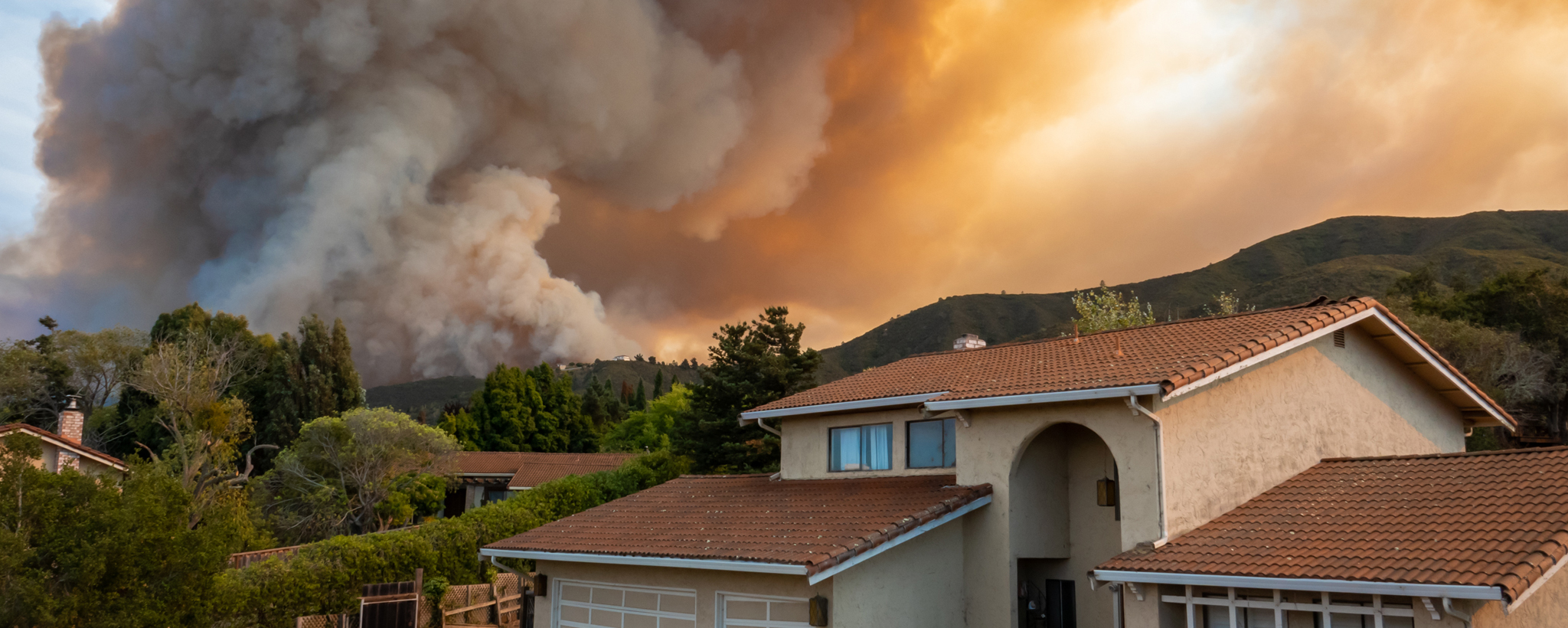 Smoke plumes from a wildfire behind a home. 