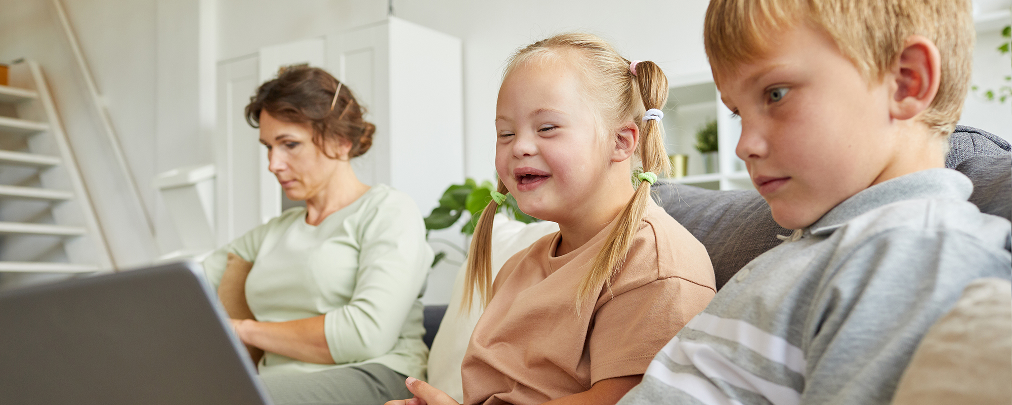 A girl with down syndrome sits on the couch with her mother and brother.