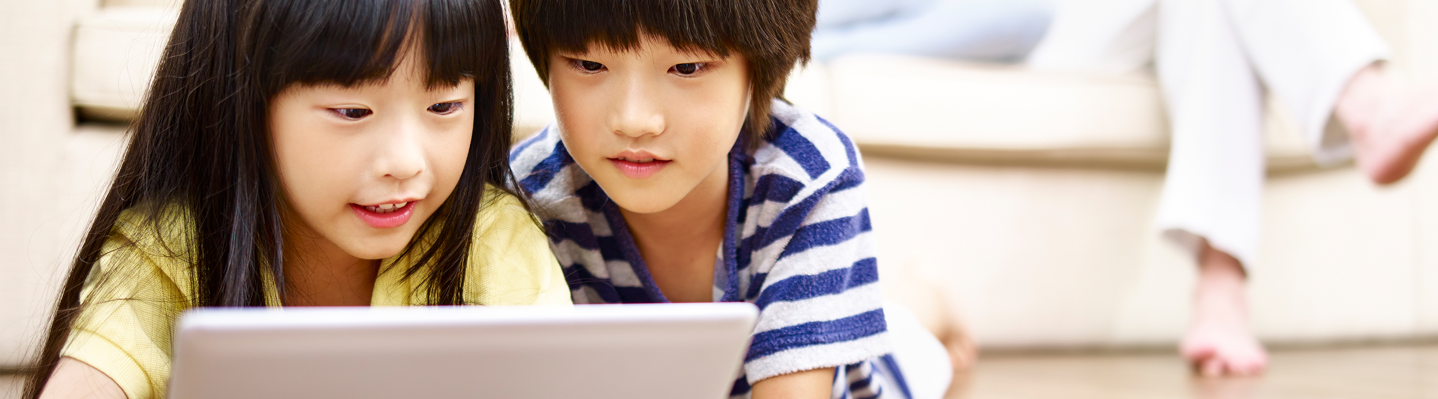 Boy and girl playing on the floor with their laptop while their parents sit on the couch in the background