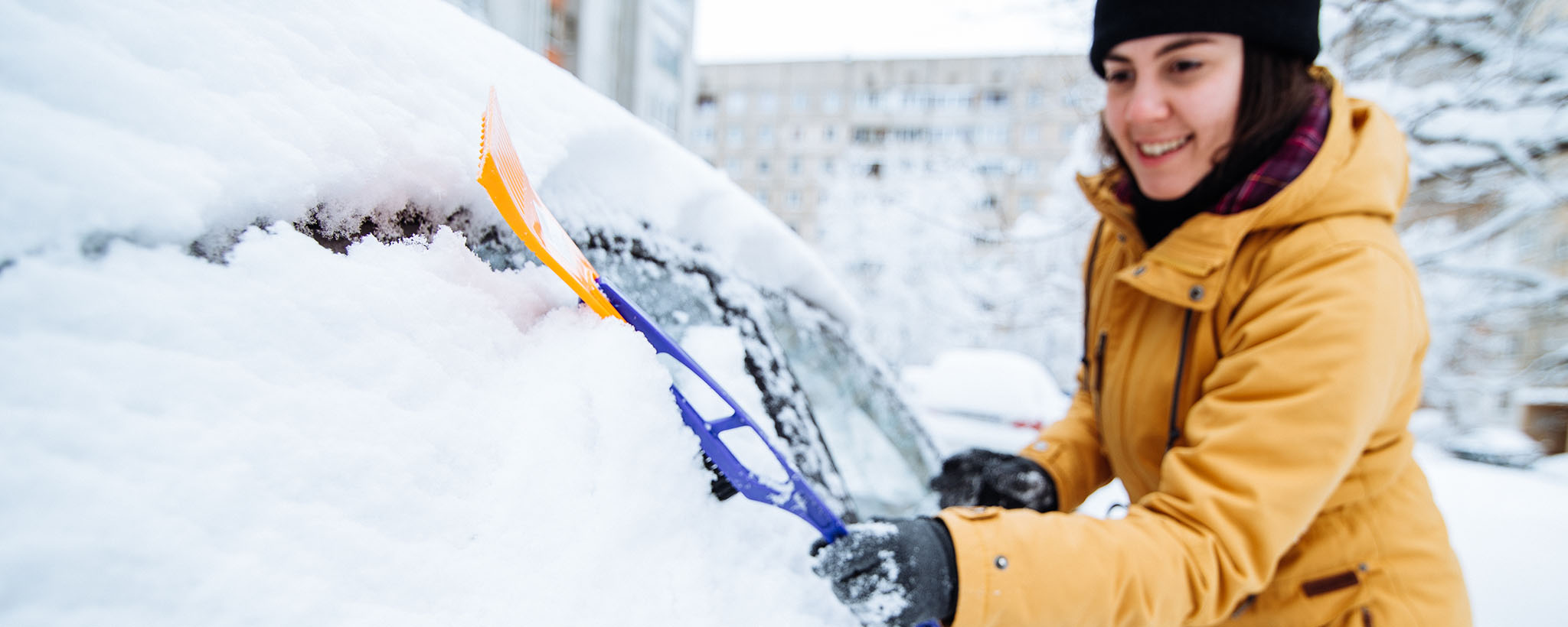 A woman scraping snow from her car. 