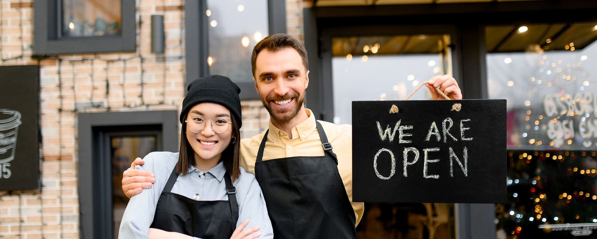 man and woman stand in front of building with open sign