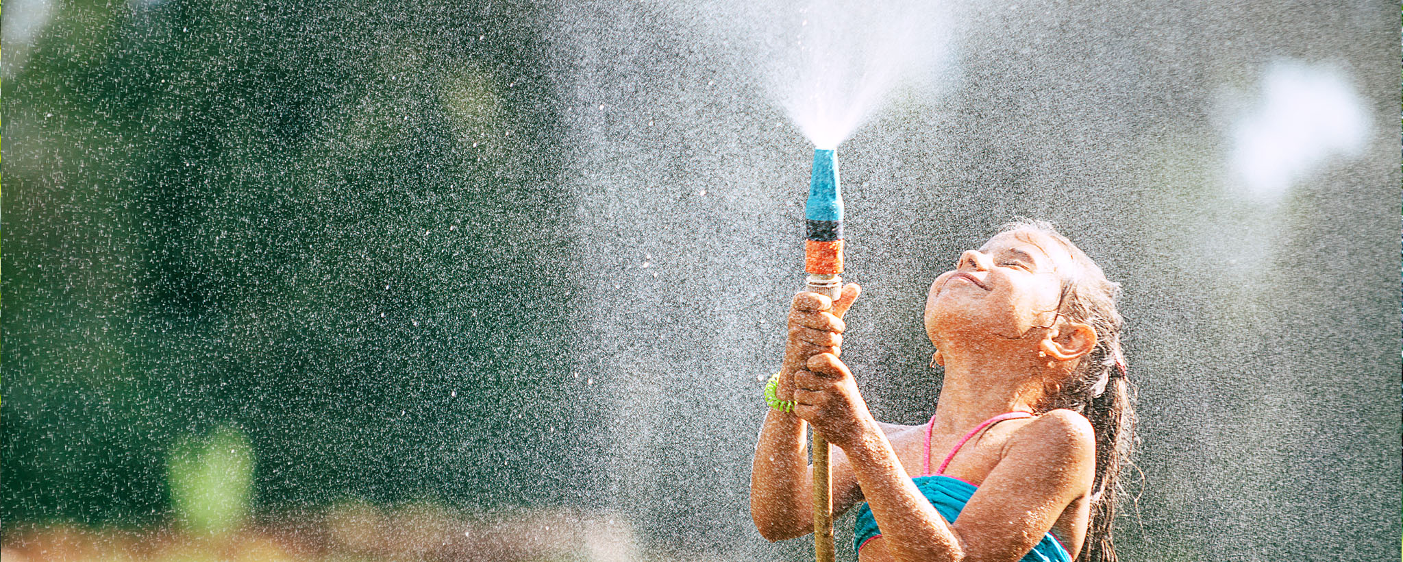 A girl using a hose as a sprinkler on a hot summer day. 