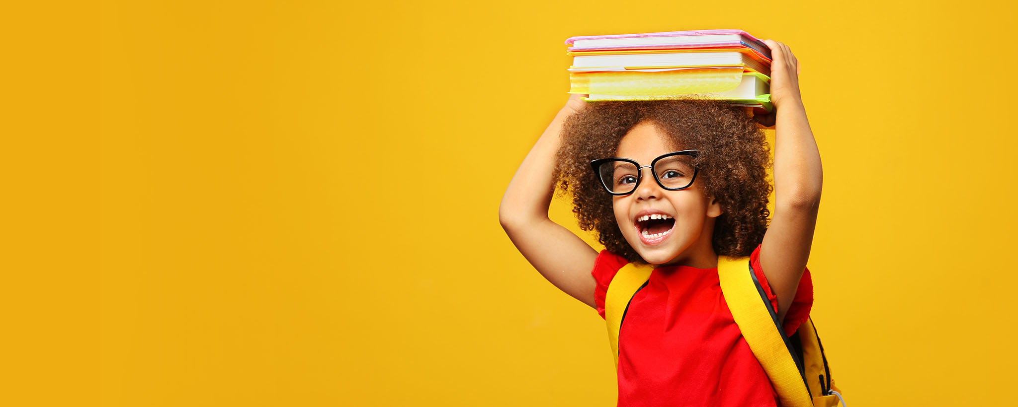 A girl wearing a backpack holds her school books on top of her head. 