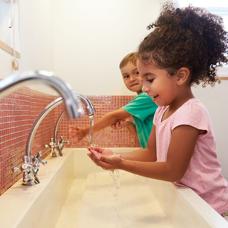 Un niño y una niña lavándose las manos en el lavabo del baño. 