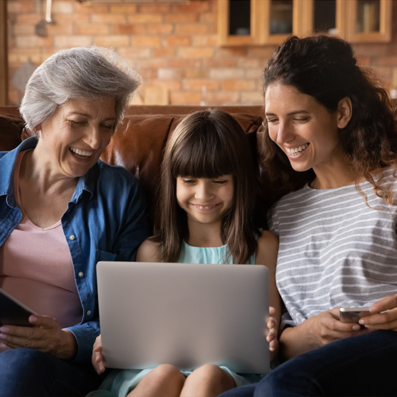 A grandmother, mother and daughter sit together looking at a laptop.