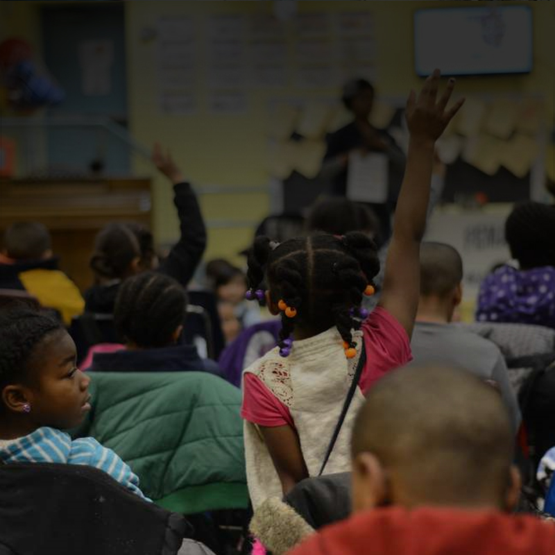 children sit on the floor, learning about preparedness. A child sitting in the middle raises her hand.