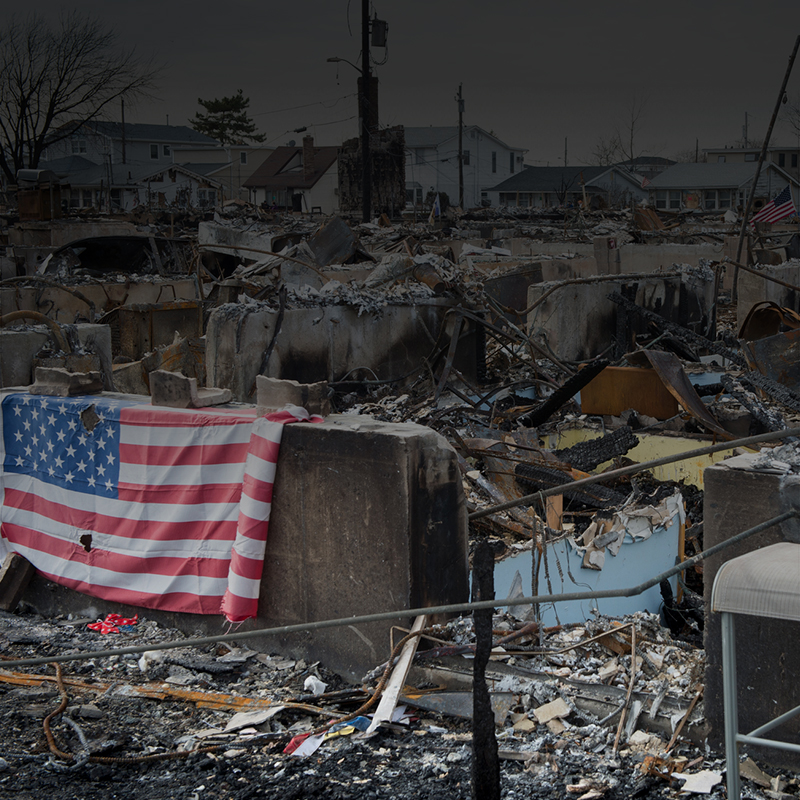 Decimated houses and rubble after hurricane Sandy, with an American flag drapped over the damage.