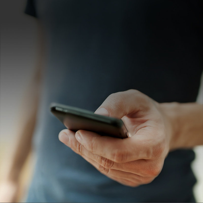 Close up photo of a man in a blue shirt holding a smart phone.