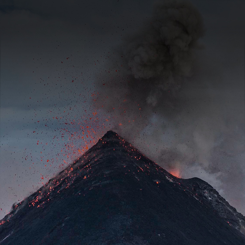 Image of an erupting volcano from up close with lava spouting everywhere and smoke coming from the top