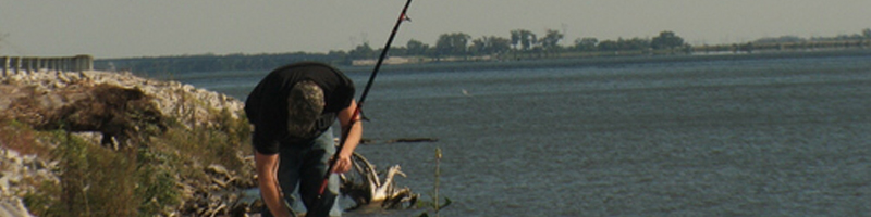 August 28th, 2005. Along the shoreline, a fisherman gets ready for the day as he pokes his cast-out pole into the sand.