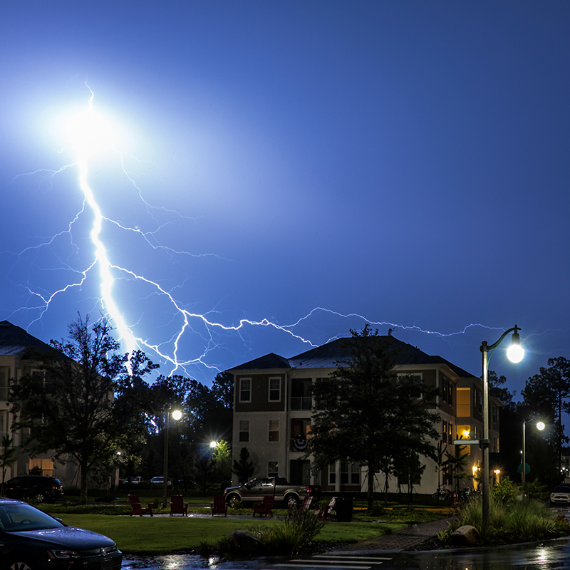 Image shows a lightning bolt striking in the background of an apartment building.