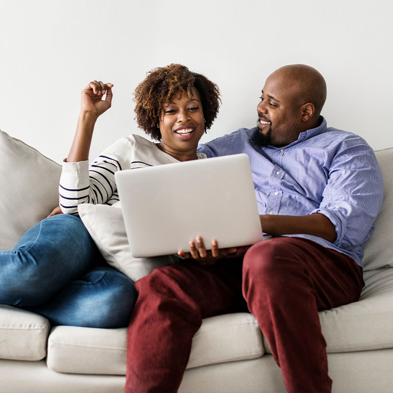 Husband and wife sitting together on the couch looking at a laptop