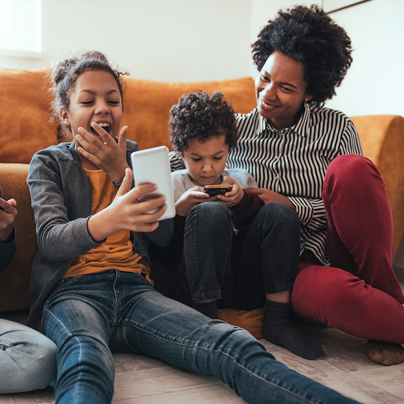 una madre sentada con sus hijos mirando sus teléfonos celulares