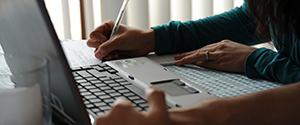 Cyber Incident- Hands writing notes from a laptop computer screen.