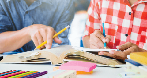 a close up of two people's hands working on school work