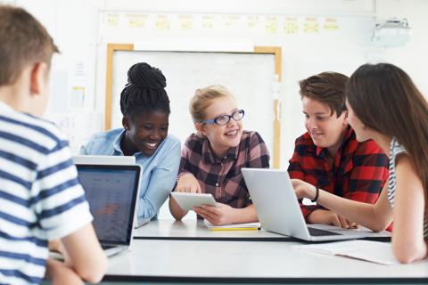 teens sitting around a table talking with laptops