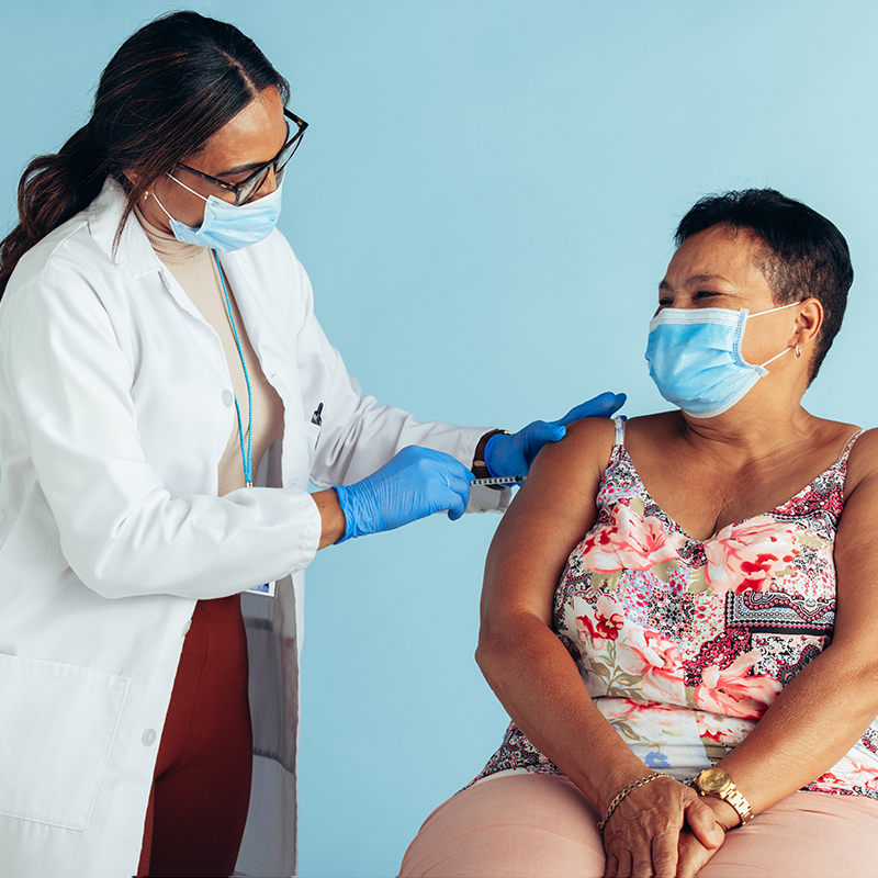 A woman wearing a mask being vaccinated by a masked medical professional.