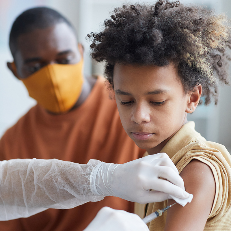 A boy getting vaccinated as his father looks on