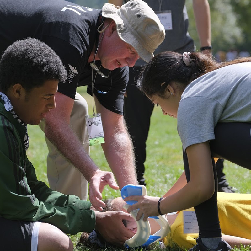 Youth preparedness council members conduct a life-saving disaster simulation exercise on a woman laying on the ground.